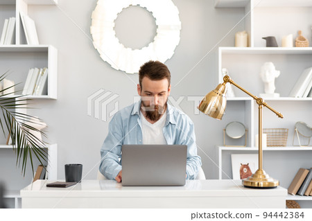Stylish bearded man working on laptop from home sitting at the table 94442384