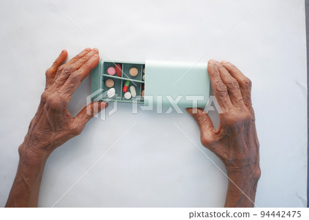senior women taking medical pills from a pill box on white background  94442475