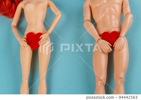 Naked male and female dolls holding red hearts covering thier groin. Love or valentines day concept. Blue background with copy space. 94442563