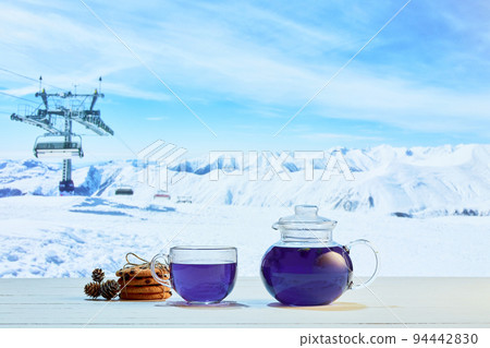 Glass pot with fruit or berries tea, cakes, biscuits on table over winter snow natural landscape background. Design for greeting card, poster for ad 94442830