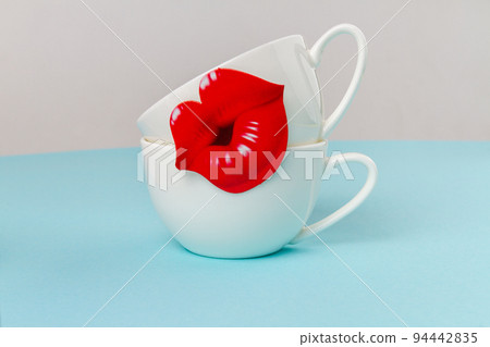 Two white ceramic cups decorated with red lips. Happy mothers day concept. Space for text. Two white ceramic cups decorated with red lips. Happy mothers day concept. Space for text. 94442835