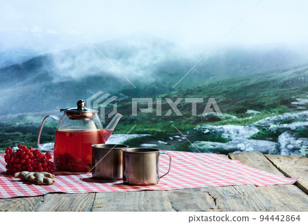 Glass pot with fruit or berries tea, cakes, biscuits on table over winter snow natural landscape background. Design for greeting card, poster for ad Glass pot with fruit or berries tea, cakes, biscuits on table over winter snow natural landscape background. Design for greeting card, poster for ad 94442864