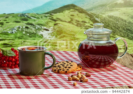 Homemade herbal or fruit tea. Glass pot, cup and sweets on wooden table over natural landscape background. Beauty, art, taste and traditions of countries Homemade herbal or fruit tea. Glass pot, cup and sweets on wooden table over natural landscape background. Beauty, art, taste and traditions of countries 94442874