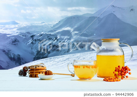 Tea with honey. Glass pot with fruit or berries tea, cakes, biscuits on table over winter snow natural landscape background. Design for greeting card 94442906