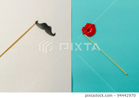 Paper moustache and lips on wooden sticks. Concept of couple or contrast. White and turquoise background. 94442970