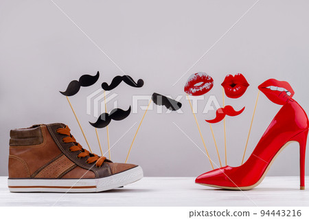 Mens and womens shoes on white background. Red High heel shoes with lips. Brown sneakers with moustache. Mens and womens shoes on white background. Red High heel shoes with lips. Brown sneakers with moustache. 94443216