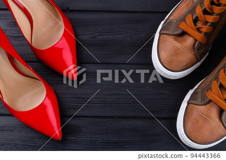 Mens shoes and red high heel womens shoes. Dark wooden background. Copy space for text. 94443366