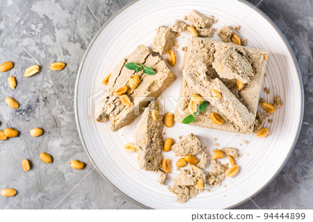 Pieces of sunflower and peanut halva and mint leaves on a plate and nuts nearby on the table. Caloric oriental delicacy. Top view. Close-up Pieces of sunflower and peanut halva and mint leaves on a plate and nuts nearby on the table. Caloric oriental delicacy. Top view. Close-up 94444899