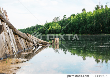 An old broken wooden fence is flooded by a flood on the river bank. Natural disaster and destruction. Beautiful landscape. 94444906