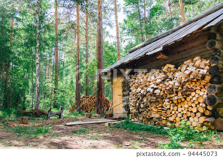 A lonely old hunter's house and a pile of firewood nearby in a forest glade in a Siberian forest A lonely old hunter's house and a pile of firewood nearby in a forest glade in a Siberian forest 94445073