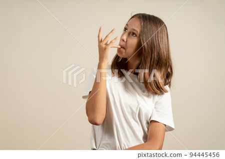 Portrait of a Latin teenage girl sucking her fingers after having eaten something delicious, isolated on beige studio background. 94445456