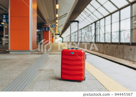 Forgotten travel bag on the train station. Red suitcase on empty station platform. Travel and vacation theme background. Travel banner Forgotten travel bag on the train station. Red suitcase on empty station platform. Travel and vacation theme background. Travel banner 94445567