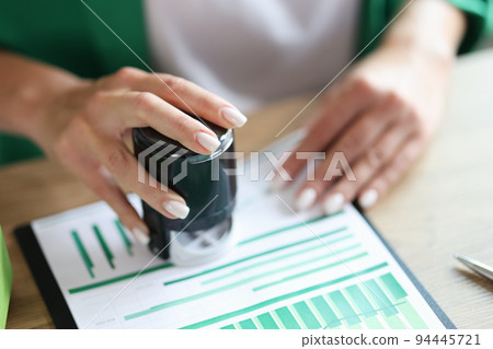 Businesswoman at table puts seal on financial documents with charts Businesswoman at table puts seal on financial documents with charts 94445721