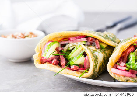 Egg rolls filled with pastrami, vegetables and green onions on a plate on the table. Hearty and high-calorie snack. Close-up Egg rolls filled with pastrami, vegetables and green onions on a plate on the table. Hearty and high-calorie snack. Close-up 94445909