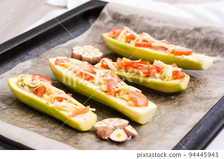 Raw zucchini halves, ready to bake, stuffed with cheese and tomato on baking paper on a baking sheet. Vegetable dishes, healthy food Raw zucchini halves, ready to bake, stuffed with cheese and tomato on baking paper on a baking sheet. Vegetable dishes, healthy food 94445943