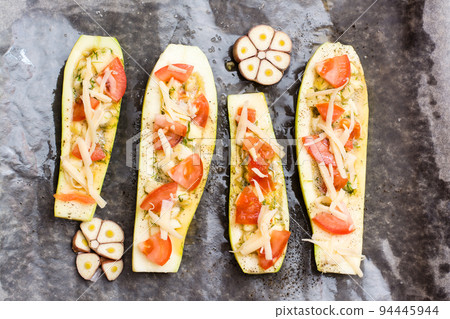 Raw zucchini halves, ready to bake, stuffed with cheese and tomato on baking paper on a baking sheet. Vegetable dishes, healthy food. Top view Raw zucchini halves, ready to bake, stuffed with cheese and tomato on baking paper on a baking sheet. Vegetable dishes, healthy food. Top view 94445944