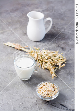 Oat milk in a cup, oatmeal and ears of corn on the table. Alternative to cow's milk. Healthy eating. Vertical view 94445961