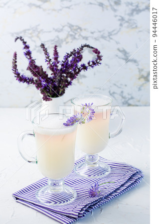 Coffee with milk, foam and lavender in glasses and a bouquet of flowers in a jug on a white table. Vertical view 94446017