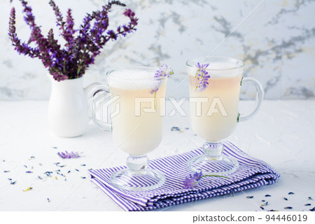Coffee with milk, foam and lavender in glasses and a bouquet of flowers in a jug on a white table 94446019