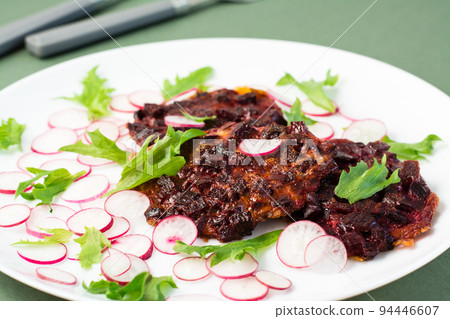 Vegetable diet food. Beetroot steak, radish and frieze salad leaves on a plate on a green background. Close-up Vegetable diet food. Beetroot steak, radish and frieze salad leaves on a plate on a green background. Close-up 94446607