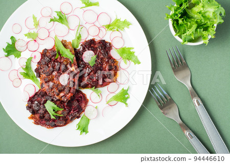 Vegetable diet food. Beetroot steak, radish and frieze salad leaves on a plate and forks  on a green background. Close-up 94446610