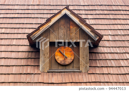 historic dormer with a wooden clock on a shingled roof 94447013