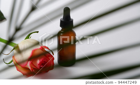 Essential oils on white background with palm leaves and rose flower, mockup. Cosmetic medical beauty product in brown glass bottles with a pipette. 94447249