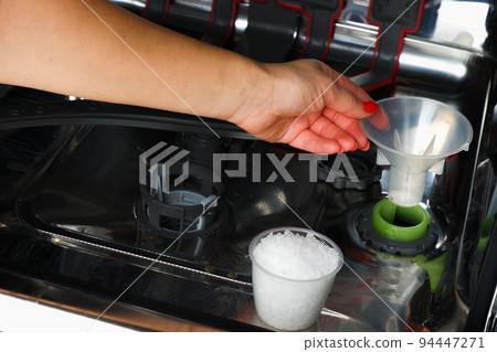 Adding salt to the dishwasher. A woman's hand pours salt to soften the water into the dishwasher. Dishwasher salt for regenerating the water softener 94447271
