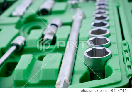Chrome mechanics tools set. Close-up photo of a set of sockets with a screwdriver and a ratchet in a green plastic case against a background of green grass. Auto tool. Chrome mechanics tools set. Close-up photo of a set of sockets with a screwdriver and a ratchet in a green plastic case against a background of green grass. Auto tool. 94447424