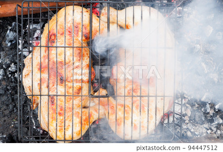 Cooking chicken meat over charcoal. Chicken meat fried with a crust on a wire rack during grill cooking. Cooking chicken meat over charcoal. Chicken meat fried with a crust on a wire rack during grill cooking. 94447512