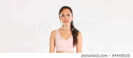 Sport, wellbeing and active lifestyle concept. Skeptical and displeased asian sportswoman, female athlete smirk disappointed and unamused, looking left with frowning face, white background Sport, wellbeing and active lifestyle concept. Skeptical and displeased asian sportswoman, female athlete smirk disappointed and unamused, looking left with frowning face, white background 94448020