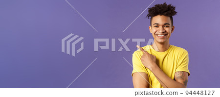 Close-up portrait of enthusiastic, happy young hipster male with dreads, beaming smile and pointing finger upper left corner, present cool product, introduce something really good, purple background Close-up portrait of enthusiastic, happy young hipster male with dreads, beaming smile and pointing finger upper left corner, present cool product, introduce something really good, purple background 94448127
