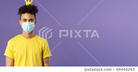 Portrait of funny hispanic guy in face mask, fool around, going crazy staying inside home during quarantine, wearing small crown and look camera, social-distancing, staying healthy covid19 pandemia 94448263