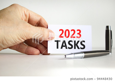 2023 Tasks symbol. White paper with words 2023 Tasks. Businessman hand. Metallic pen. Beautiful white table white background. Business and 2023 tasks concept. Copy space. 2023 Tasks symbol. White paper with words 2023 Tasks. Businessman hand. Metallic pen. Beautiful white table white background. Business and 2023 tasks concept. Copy space. 94448430