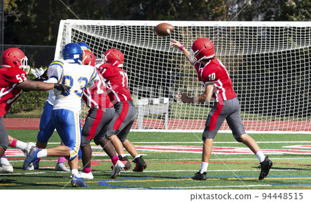 Football quarterback passing the ball over his lineman Football quarterback passing the ball over his lineman 94448515