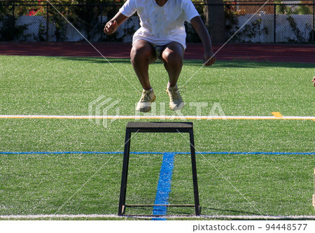 Athlete landing on a tall plyo box that is on a turf field Athlete landing on a tall plyo box that is on a turf field 94448577