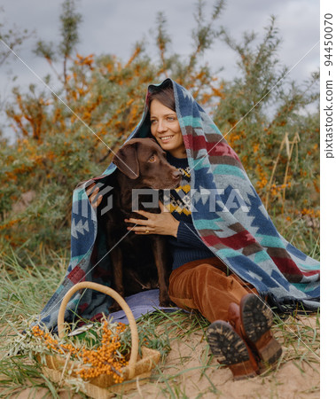 woman and a Labrador retriever dog on a picnic, a cozy walk and hugs. a young woman and a pet collect sea buckthorn 94450070