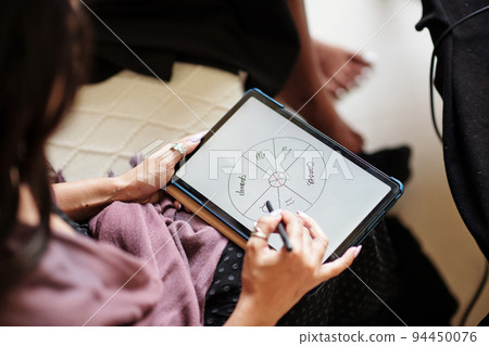 Close-up image of astrologer drawing natal card on tablet computer 94450076