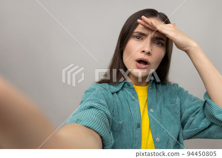 Portrait of astonished woman with amazed face expression, making selfie, looking far away, point of view photo, wearing casual style jacket. Indoor studio shot isolated on gray background. 94450805