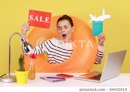 Joyful woman with rubber ring, holding card with sale inscription, passport and paper plane, rejoice sales for summer tours. Indoor studio studio shot isolated on yellow background. Joyful woman with rubber ring, holding card with sale inscription, passport and paper plane, rejoice sales for summer tours. Indoor studio studio shot isolated on yellow background. 94450919