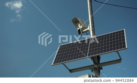 Photo camera monitors the rules of the road. Camera on a pole with a solar panel against the sky. Photo camera monitors the rules of the road. Camera on a pole with a solar panel against the sky. 94452884