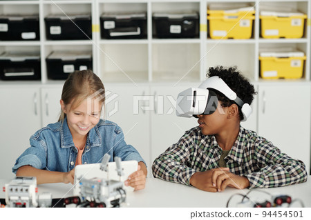 Two clever intercultural schoolkids playing virtual game at lesson of robotics Two clever intercultural schoolkids playing virtual game at lesson of robotics 94454501