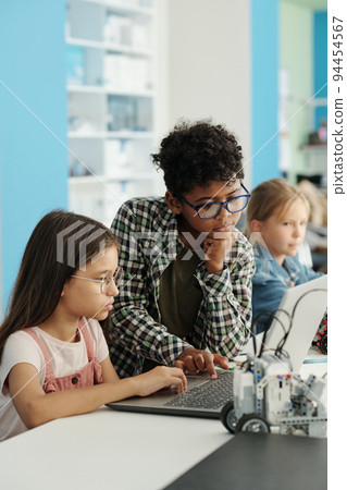 Two youthful schoolkids in casualwear and eyeglasses looking at laptop screen Two youthful schoolkids in casualwear and eyeglasses looking at laptop screen 94454567
