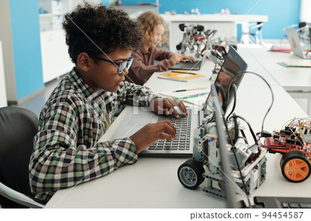 Side view of clever African American schoolboy sitting in front of laptop 94454587