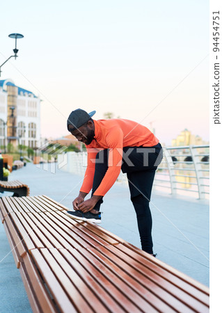 Side view of young African American man in activewear tying shoelace on sneaker Side view of young African American man in activewear tying shoelace on sneaker 94454751