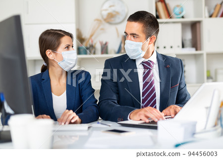 Male and female business partners in masks working in office 94456003