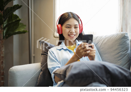 Young asian woman smiling listening to music using smartphone at home. Young asian woman smiling listening to music using smartphone at home. 94456323