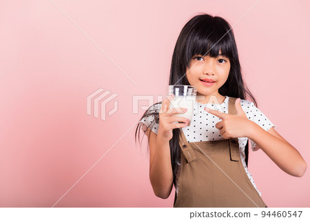 Asian little kid 10 years old smile hold milk glass drink white milk and pointing finger Asian little kid 10 years old smile hold milk glass drink white milk and pointing finger 94460547