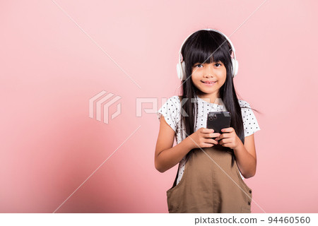 Asian kid 10 years enjoying listening music from mobile phone wear wireless headset 94460560