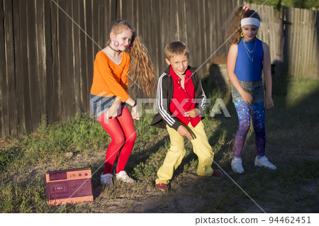 Retro kids. Two girls mi boy dressed in the style of the nineties are dancing to a retro tape recorder. Retro kids. Two girls mi boy dressed in the style of the nineties are dancing to a retro tape recorder. 94462451